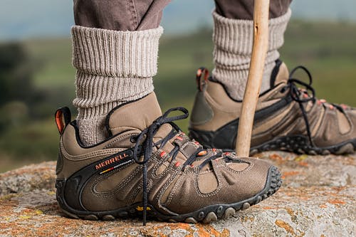 男式棕色和灰色merrell远足鞋拿着棍子 · 免费素材图片