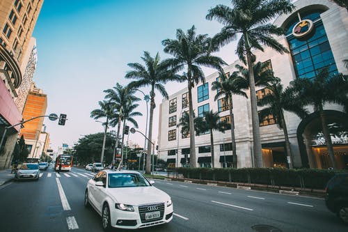 白色奥迪轿车在灰色的混凝土道路上，周围绿树环绕的混凝土建筑 · 免费素材图片