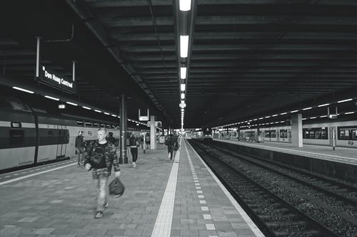 在地铁站上走的人背着书包的灰度摄影 · 免费素材图片