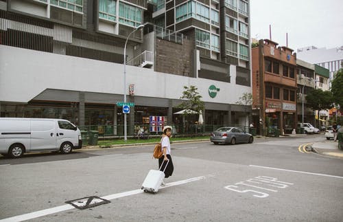 女人走向大楼时拉行李箱 · 免费素材图片