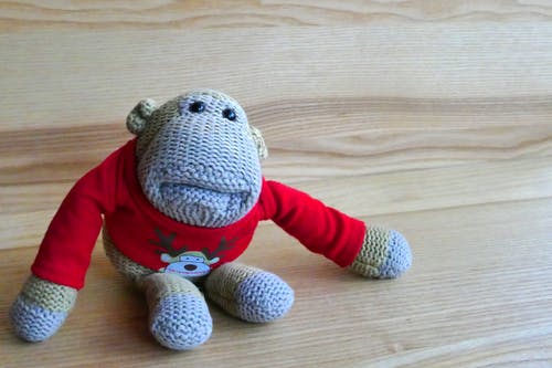 灰色的猴子amigurumi娃娃在棕色的木质表面上穿红色的毛衣 · 免费素材图片