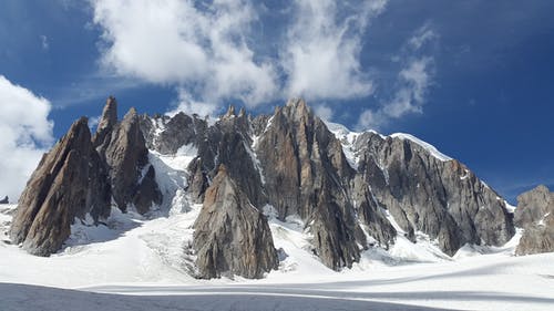 白天在蓝蓝的天空下白雪覆盖的岩石山 · 免费素材图片