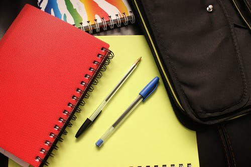 红色盖的笔记本旁边的黑色和蓝色笔 · 免费素材图片