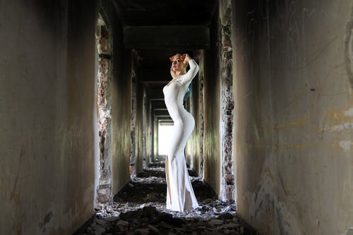 在白色的混凝土墙之间张贴的白色紧身衣长连衣裙的女人 · 免费素材图片