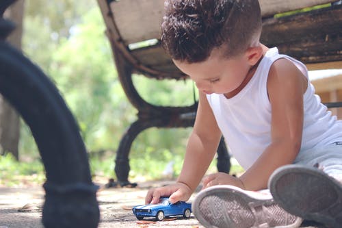 白天玩蓝色小轿车模具的白色背心的男孩铸成棕色木制长椅附近 · 免费素材图片