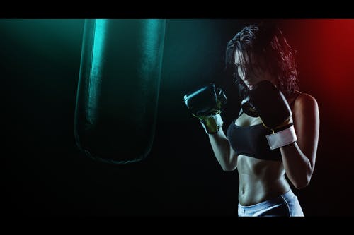 拳击手套与运动胸罩摆在出气筒前拳击风格的女人 · 免费素材图片