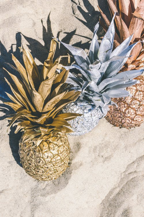 在沙滩上的三个彩绘的菠萝果实的特写照片 · 免费素材图片
