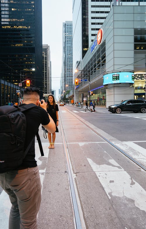 男子拍照的女人站在大楼附近公路旁的照片 · 免费素材图片