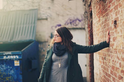 穿绿色外套的女人靠在墙上的左手 · 免费素材图片