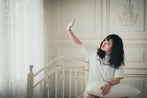 女人坐在床上举起右手在房间里 · 免费素材图片