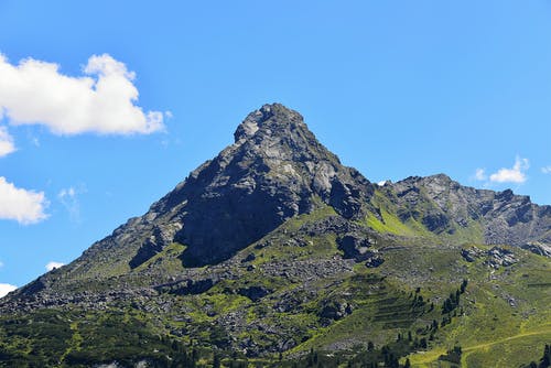 在晴朗的蓝天和白云下绿树覆盖的灰山 · 免费素材图片