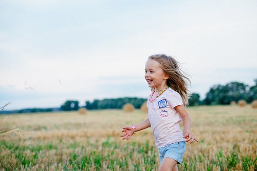 在绿色的原野上向左奔跑的小女孩微笑着 · 免费素材图片