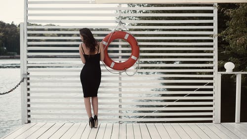 码头游泳圈旁边的黑色外套的女人 · 免费素材图片