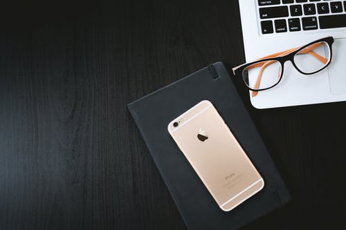 黑色保护套上的金色iphone 6以及银色macbook上的眼镜 · 免费素材图片