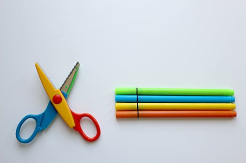 多彩多姿的剪刀和白色表面上的四种着色笔 · 免费素材图片
