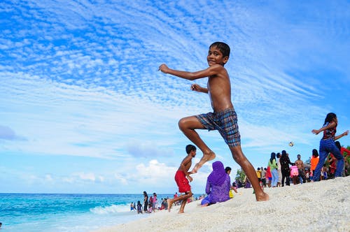 在海洋附近的白色沙滩上跳跃的男孩 · 免费素材图片
