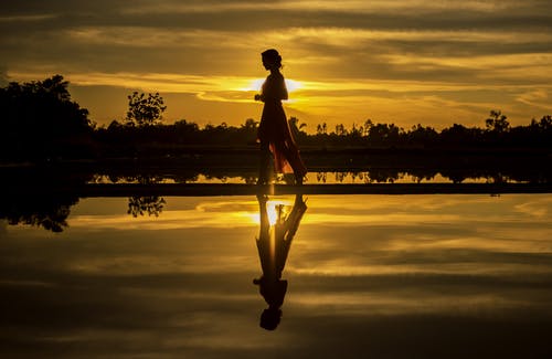 男子站在湖上在日落时的剪影 · 免费素材图片
