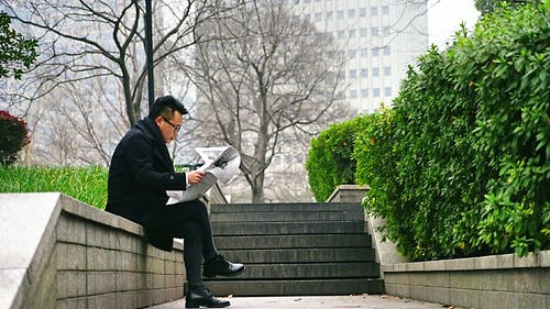 坐在楼梯墙上的男人读报纸 · 免费素材图片