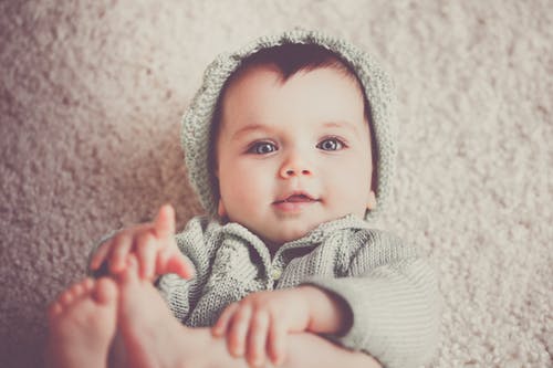 婴儿躺在地毯上的灰色针织连帽的衣服 · 免费素材图片