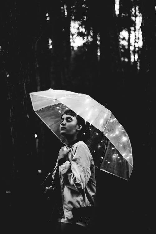 女人拿着雨伞走在雨中的灰度图像 · 免费素材图片