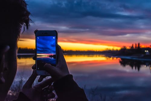 拿着智能手机的人在金黄小时下拍湖照片 · 免费素材图片