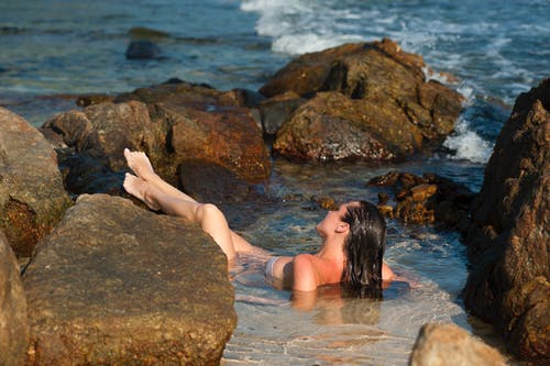 女人在岩石旁边游泳 · 免费素材图片