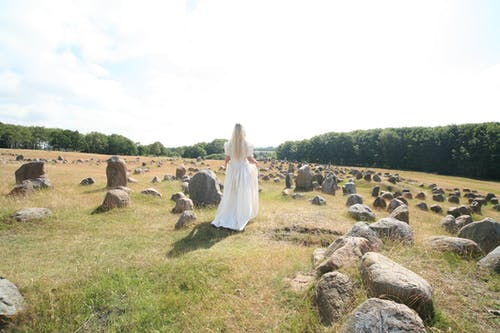 女人穿着长礼服站在岩石附近 · 免费素材图片