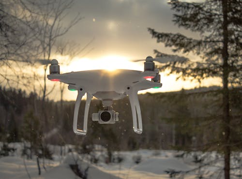 白色无人机quadcopter在中午在树附近飞行的照片 · 免费素材图片
