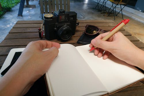 在单反相机旁边棕色木制的桌子上写的人 · 免费素材图片