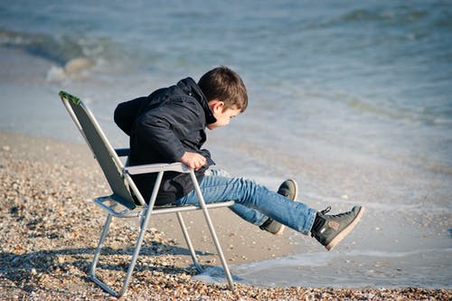 男孩坐在海边的椅子上 · 免费素材图片