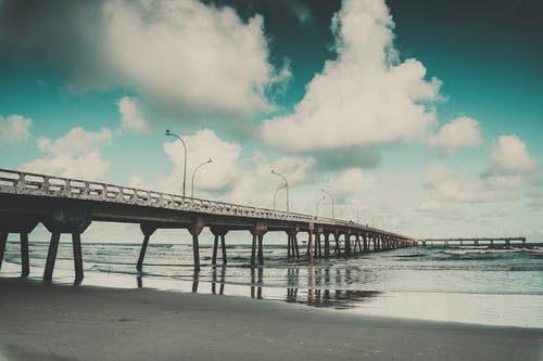 白云和灰色混凝土桥附近在海边 · 免费素材图片