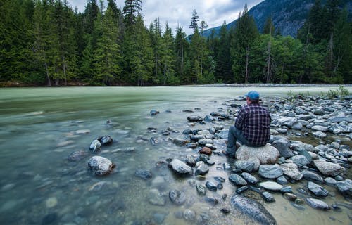 坐在水边的石头上的人 · 免费素材图片