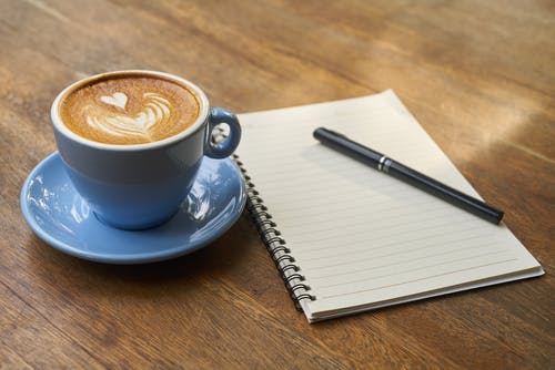 茶碟在笔记本旁边的咖啡 · 免费素材图片