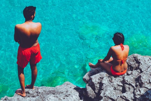男人和女人站立和坐在悬崖附近的水体 · 免费素材图片