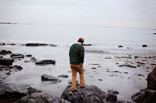 男子站在水体附近的岩层上 · 免费素材图片