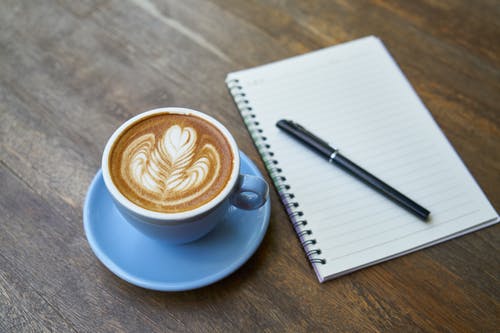杯拿铁咖啡在螺旋笔记本旁边 · 免费素材图片