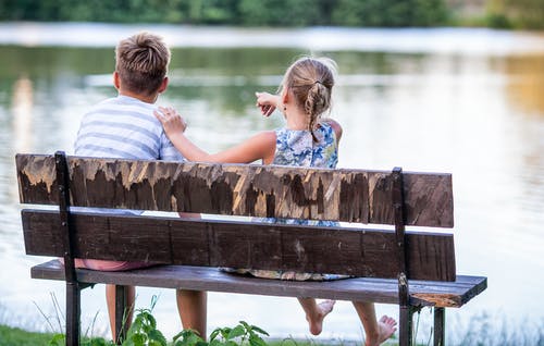 男孩和女孩坐在湖边的长椅上的选择性聚焦摄影 · 免费素材图片
