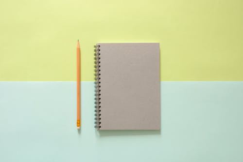 橙色铅笔旁边的白色螺旋笔记本 · 免费素材图片