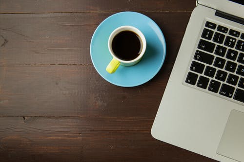 白色陶瓷杯子装满咖啡在便携式计算机旁边 · 免费素材图片