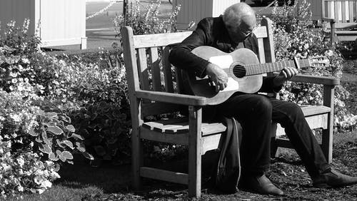 人在长椅上弹吉他的灰度照片 · 免费素材图片