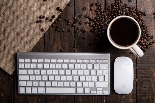 苹果魔术键盘，鼠标和杯子装满咖啡豆后的平躺摄影 · 免费素材图片