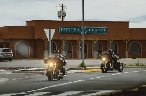 两名男子骑在彩绘的沙漠商店附近的旅游摩托车上 · 免费素材图片