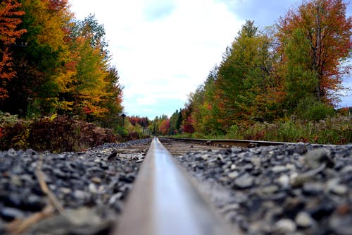 黑色钢火车轨道与鹅卵石和树木 · 免费素材图片