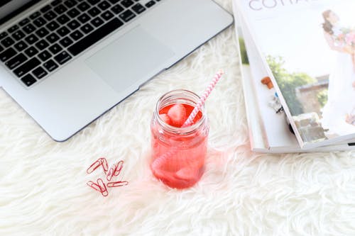 杂志和笔记本电脑旁边的一杯饮料的平躺照片 · 免费素材图片