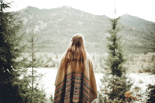 女人穿着棕色雨披面对山 · 免费素材图片