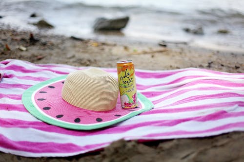条纹的毛巾铺在沙滩上，戴着草帽和果汁罐 · 免费素材图片