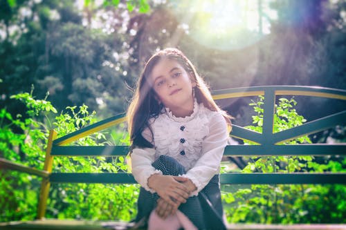 女孩坐在植物附近的长椅上 · 免费素材图片