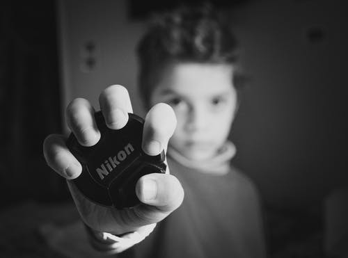 男孩拿着尼康镜头盖的选择性聚焦摄影 · 免费素材图片