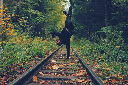 男子用右手站在森林中间的火车铁轨上 · 免费素材图片
