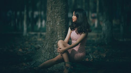 女人穿着粉红色的连衣裙，坐在树的根上的选择性焦点摄影 · 免费素材图片